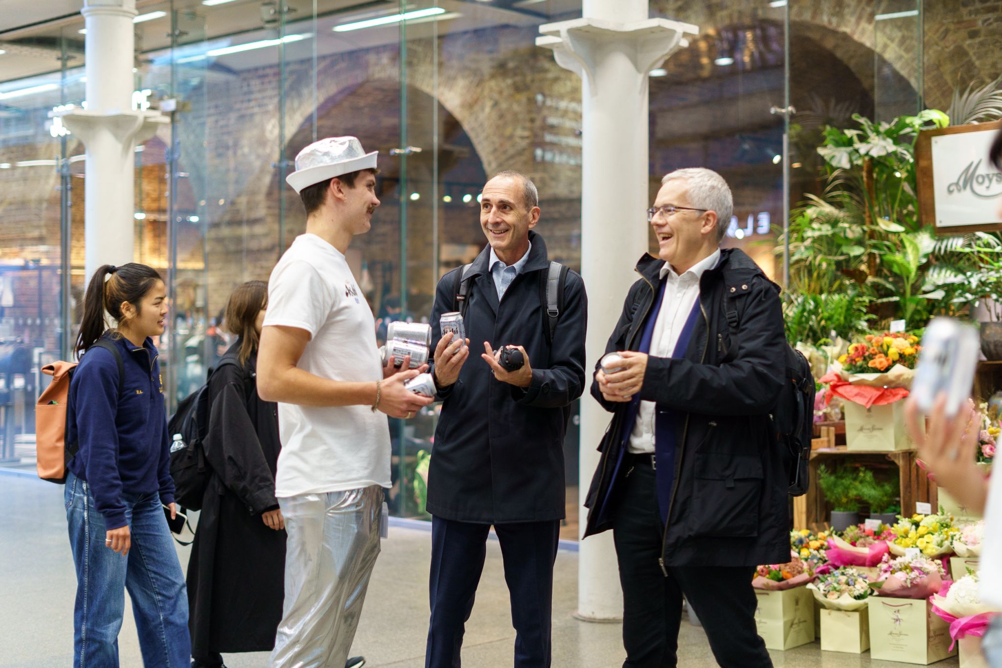 Brand ambassador in a silver hat handing cans of Asahi 0.0% beer to commuters in a busy station