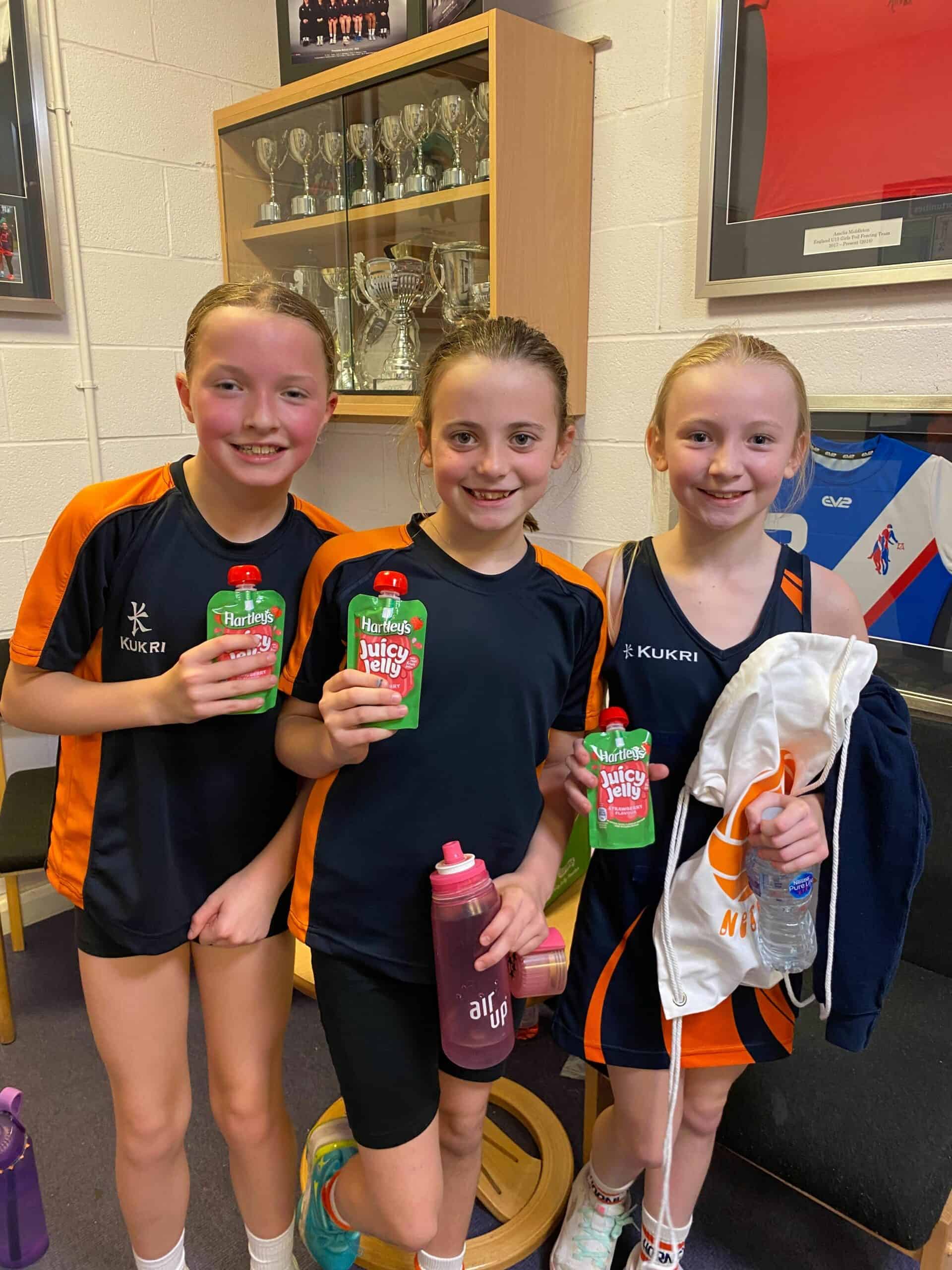 Young girls in sports uniforms smiling with juice drinks.