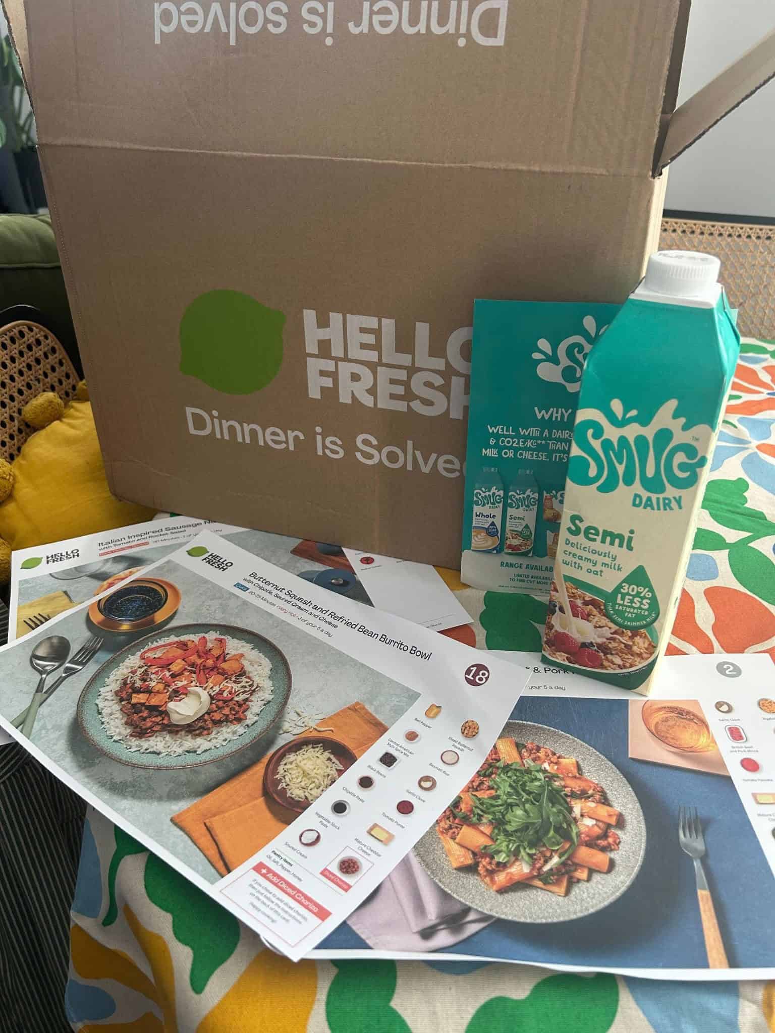 Fresh meal sample box with menu cards and milk carton on table.