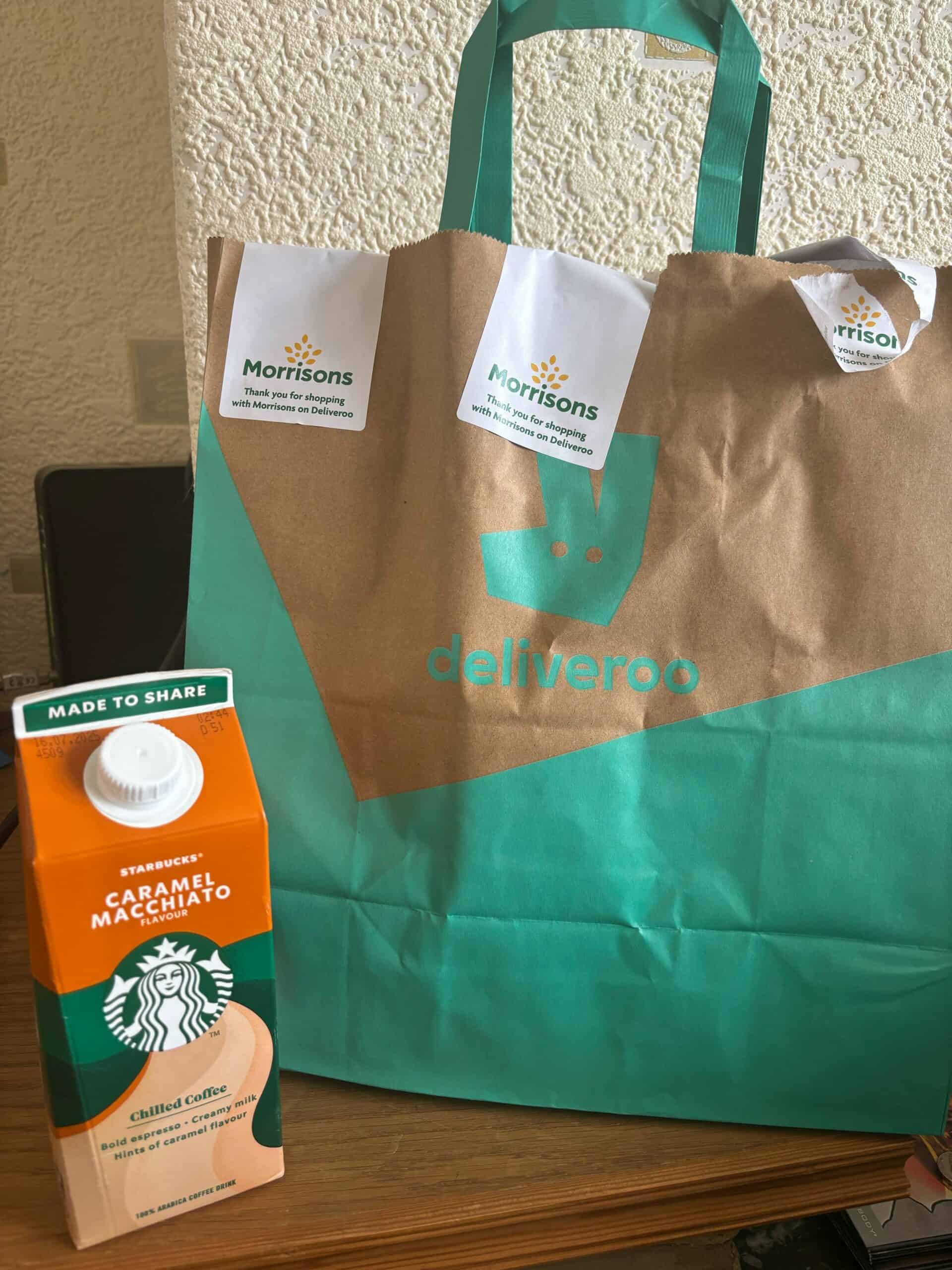 Delivery grocery bag with Starbucks Caramel Macchiato carton and Morrisons shopping tags.